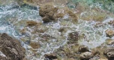 Turkuaz deniz dalgaları taşlı kıyıya sıçrayan, üst görünümü. Güzel doğal arka plan 4k