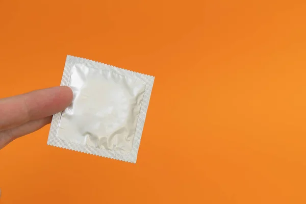 Man hand hålla en folie kondom paket, orange bakgrund — Stockfoto