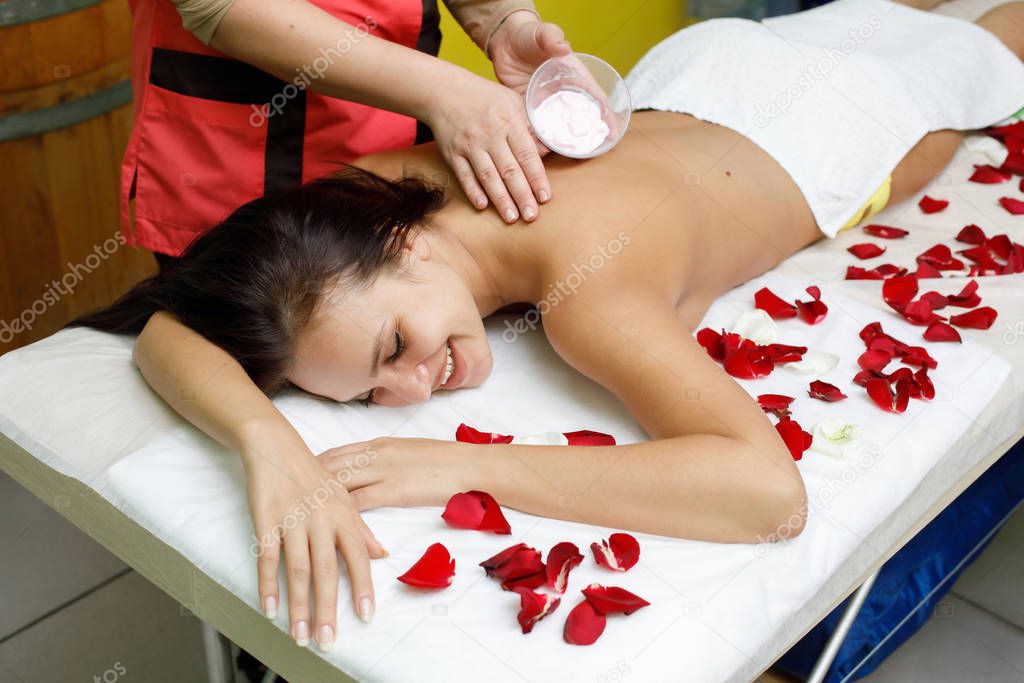 Masseur applying cream to woman's back. Massage in spa salon