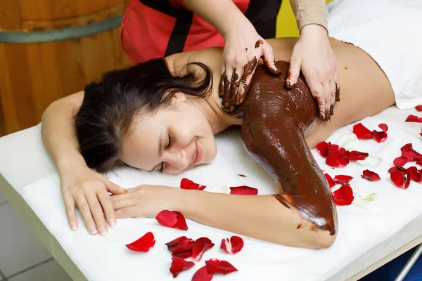 Massagista a aplicar chocolate nas costas da mulher. Massagem no salão de spa — Fotografia de Stock