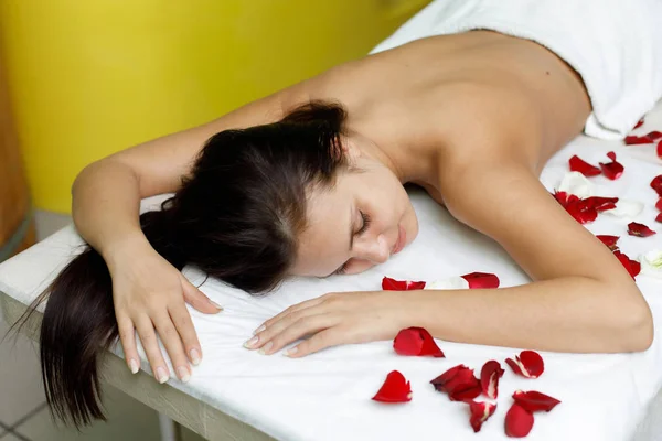 Mulher descansando no salão de beleza com pétalas de rosa — Fotografia de Stock