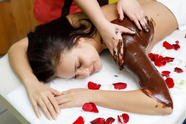 Massagista a aplicar chocolate nas costas da mulher. Massagem no salão de spa — Fotografia de Stock