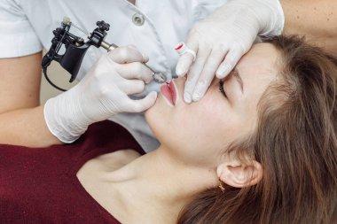 Dudaklarda kalıcı makyaj. Kozmetik uzmanı makineyle dövme yapıyor.