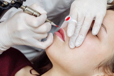 Dudaklarda kalıcı makyaj. Kozmetik uzmanı makineyle dövme yapıyor.