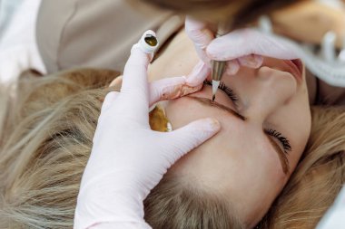 Kalıcı makyaj, kaş dövmesi. Beyaz eldivenli kozmetolog güzellik salonundaki kadının makyaj makinesiyle makyaj yapıyor.