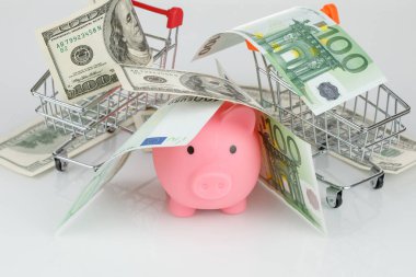 Pink piggy money box in pile of dollar and euro banknotes on gray background