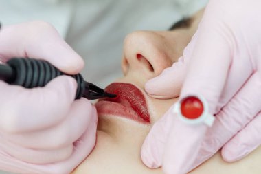 Güzellik salonunda dudaklarında kalıcı makyaj yapan bir kadın. Eldiven takan kozmetik uzmanı makine ve makro görüşlü dövme yapıyor.