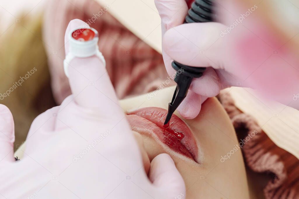 Woman having permanent makeup on lips in beauty salon. Cosmetologist in gloves applying tattoo with machine, macro view