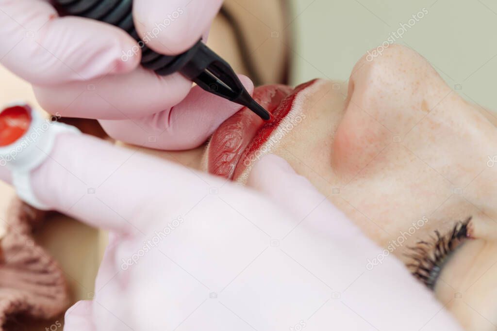 Woman having permanent makeup on lips in beauty salon. Cosmetologist in gloves applying tattoo with machine, macro view