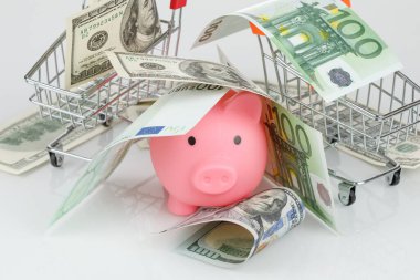 Pink piggy money box in pile of dollar and euro banknotes on gray background