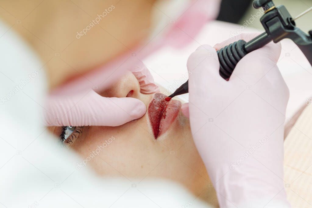 Woman having permanent makeup on lips in beauty salon. Cosmetologist in gloves applying tattoo with machine, macro view