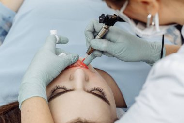 Güzellik salonunda dudaklarında kalıcı makyaj yapan bir kadın. Eldiven takan kozmetik uzmanı makine ve makro görüşlü dövme yapıyor.