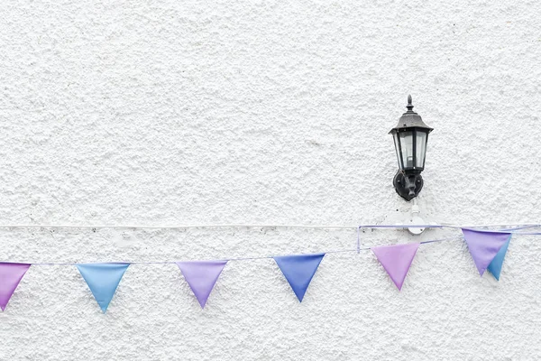 Colorful Party flags bunting hanging on white wall background with wall lamp light. Minimal hipster style design