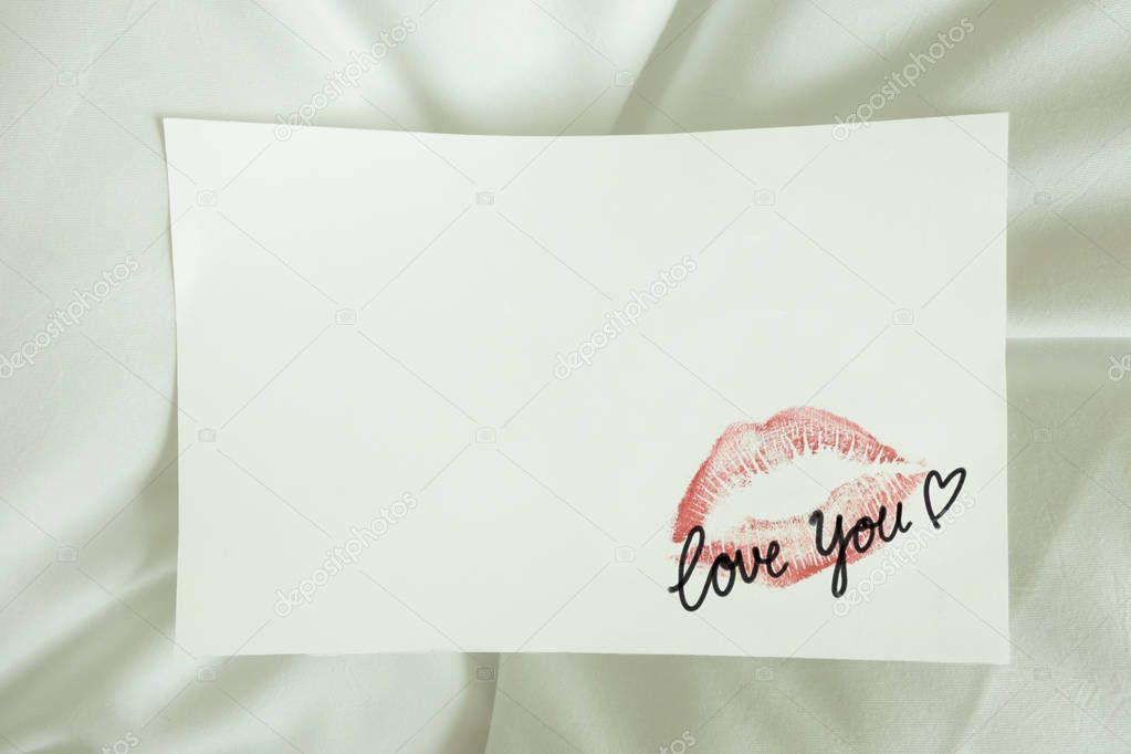 sexy red lipstick kiss 'LOVE YOU' heart on white note. white bed pillow sheet in the morning light, valentine's day.