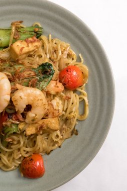 Mie goreng, kızarmış sarı şehriye. karides deniz ürünleri sebze domates choy yumurta sarımsak soğancık soğan karides lahana ile gri plaka beyaz masa örtüsü üzerinde. Lezzetli ünlü Endonezya Malezya baharatlı yemek.