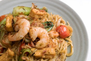 Mie goreng, kızarmış sarı şehriye. karides deniz ürünleri sebze domates choy yumurta sarımsak soğancık soğan karides lahana ile gri plaka beyaz masa örtüsü üzerinde. Lezzetli ünlü Endonezya Malezya baharatlı yemek.