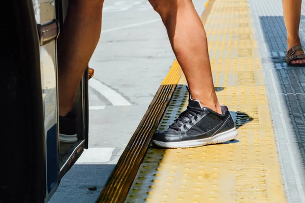 Legs of a man with sneakers getting on a bus