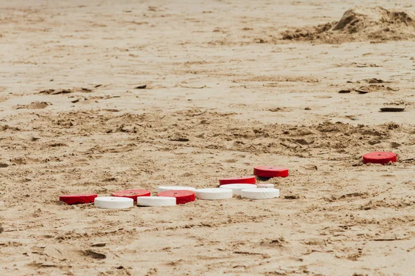 Red and white tejo discs game on beach sand