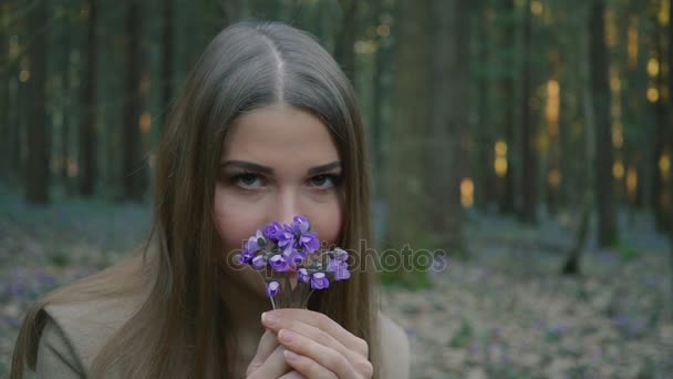Красива молода дівчина пахне весняними квітами в лісі — стокове відео