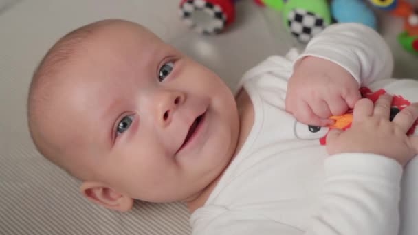 A cute little baby is looking into the camera and is happy on a white bed sheet. — Stock Video