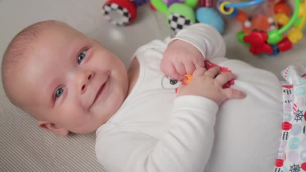 Un petit bébé mignon regarde dans la caméra et est heureux sur un drap de lit blanc . — Video