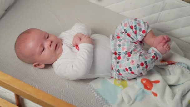 Un bebeluș drăguț se uită în cameră și este fericit pe o foaie de pat albă . — Videoclip de stoc