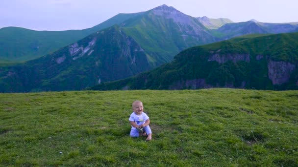 Baby speelt in de bergen, zitten en glimlachen — Stockvideo