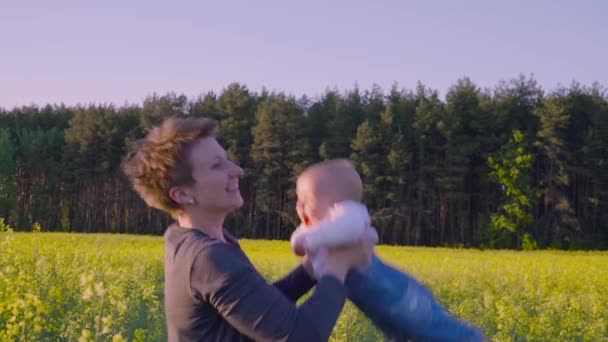 Mamá jugó con el bebé en el campo de colza y lo lanza . — Vídeos de Stock