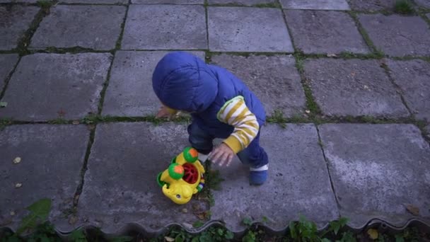 El niño en el chaleco se arrastra sobre la baldosa en la calle — Vídeos de Stock
