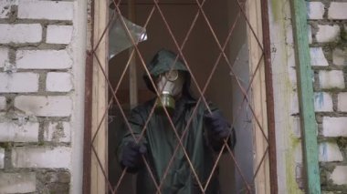 Bir gaz maskesi olan bir adam penceresinden çubuklarıyla görünüyor ve ücretsiz devam edemez
