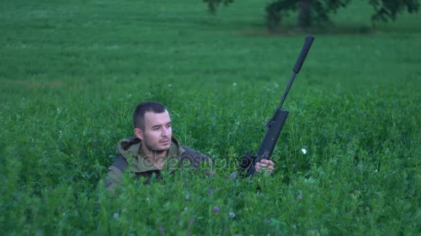 Hombre con un arma sentada en la hierba alta — Vídeos de Stock