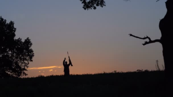 Hombre con un arma camina contra el fondo del amanecer — Vídeos de Stock