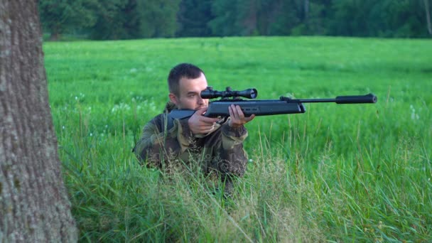 Muž s puškou na lovu vykukoval za pomalý strom — Stock video