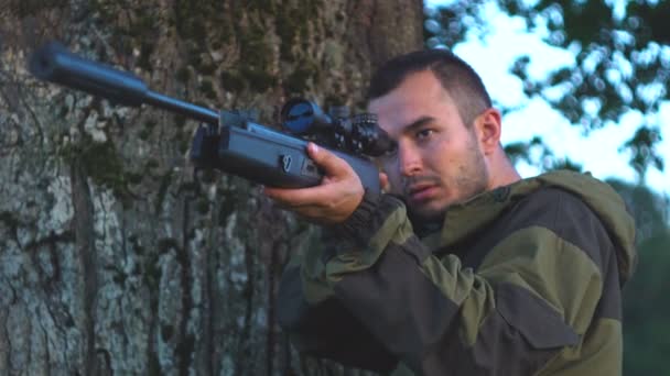 Homem com uma arma na caça atrás de uma árvore 4k — Vídeo de Stock