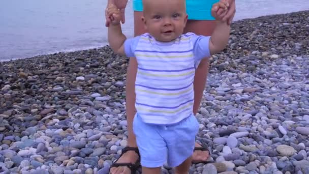 男の子の赤ちゃんを持つお母さんは、ビーチに沿って歩く — ストック動画