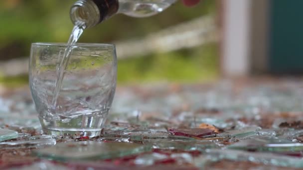 Versando vodka in un bicchiere sullo sfondo di vetro rotto — Video Stock