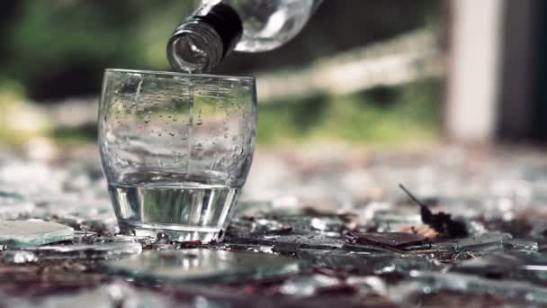 Versando vodka in un bicchiere sullo sfondo di vetro rotto — Video Stock