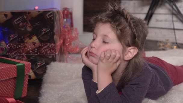 A menina se encontra perto dos presentes de Natal, olhares e sorrisos — Vídeo de Stock