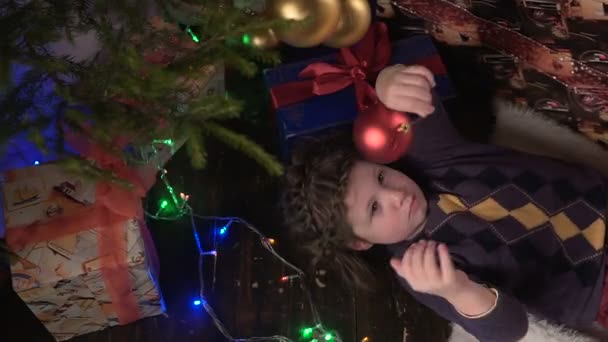 Das Mädchen liegt neben dem Weihnachtsbaum, schaut und lächelt — Stockvideo