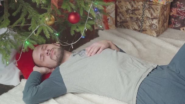 Sleepy young man near the Christmas tree — Stock Video