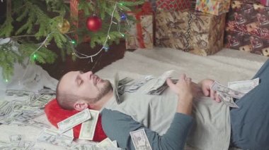 Bir adam bir sürü dolar ve bir Noel ağacı ile uyuyor