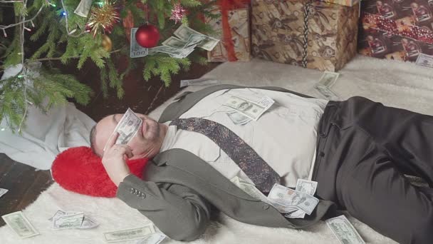 En man sover med en massa dollar och en julgran — Stockvideo