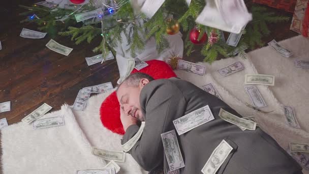 Geld fällt auf Mann, der in der Nähe eines Weihnachtsbaums schläft — Stockvideo