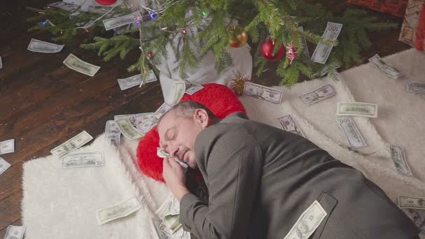 Un hombre duerme con muchos dólares y un árbol de Navidad. — Vídeo de stock