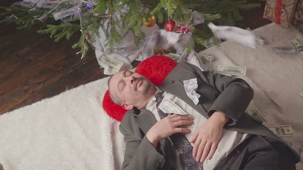 Dinheiro cai sobre um homem dormindo perto de uma árvore de Natal — Vídeo de Stock