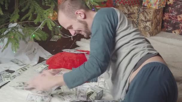 En man sover med en massa dollar och en julgran — Stockvideo