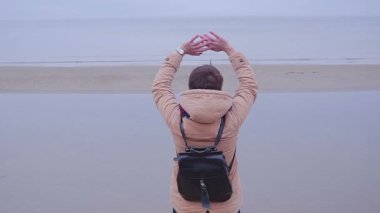 Kız deniz kıyısında ve elini sallayarak