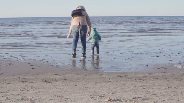 Mutter mit kleinem Kind spaziert am Frühlingsstrand entlang — Stockvideo