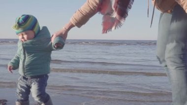 Küçük bir çocuk ile anne bahar plaj boyunca yürür