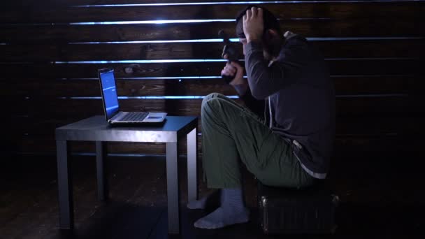 Hacker engraçado cômico comete um ataque cibernético com um laptop e uma arma em suas mãos — Vídeo de Stock